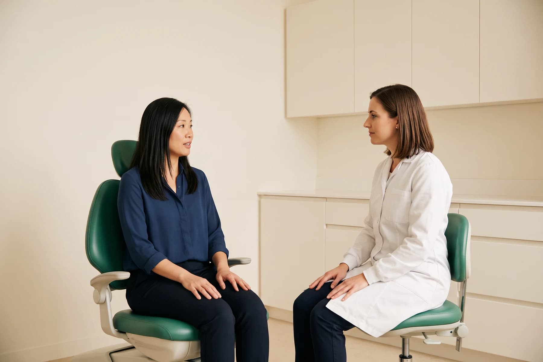 A woman in a navy blouse talks with a dentist in a bright ivory treatment room.
