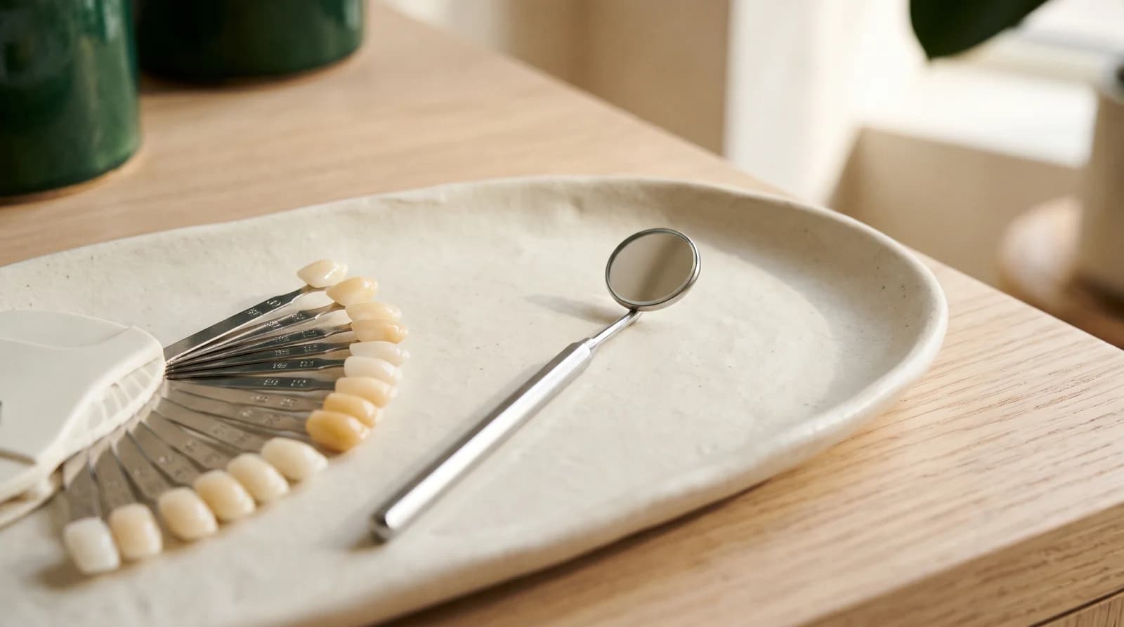 Tooth-shade tabs and a stainless dental mirror on an ivory tray.