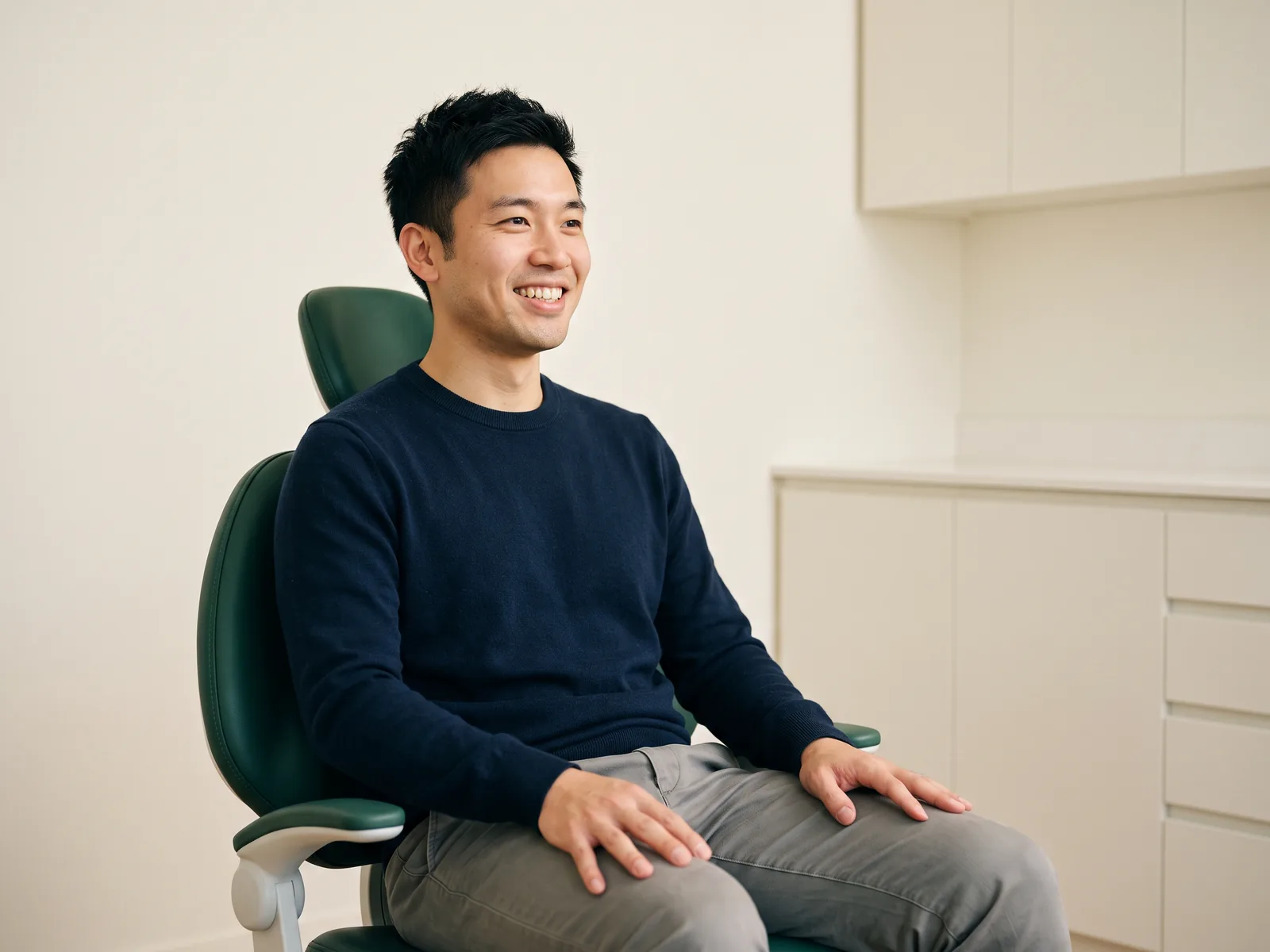Man with short dark hair and a navy sweater smiling in a green dental chair.