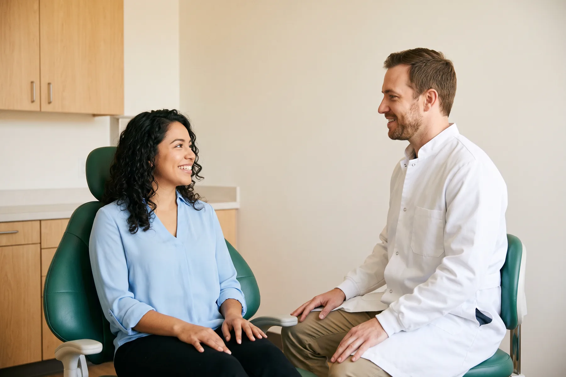 Illustrative dental conversation with a smiling woman with curly hair in a sky blue blouse and a dentist in a white coat.