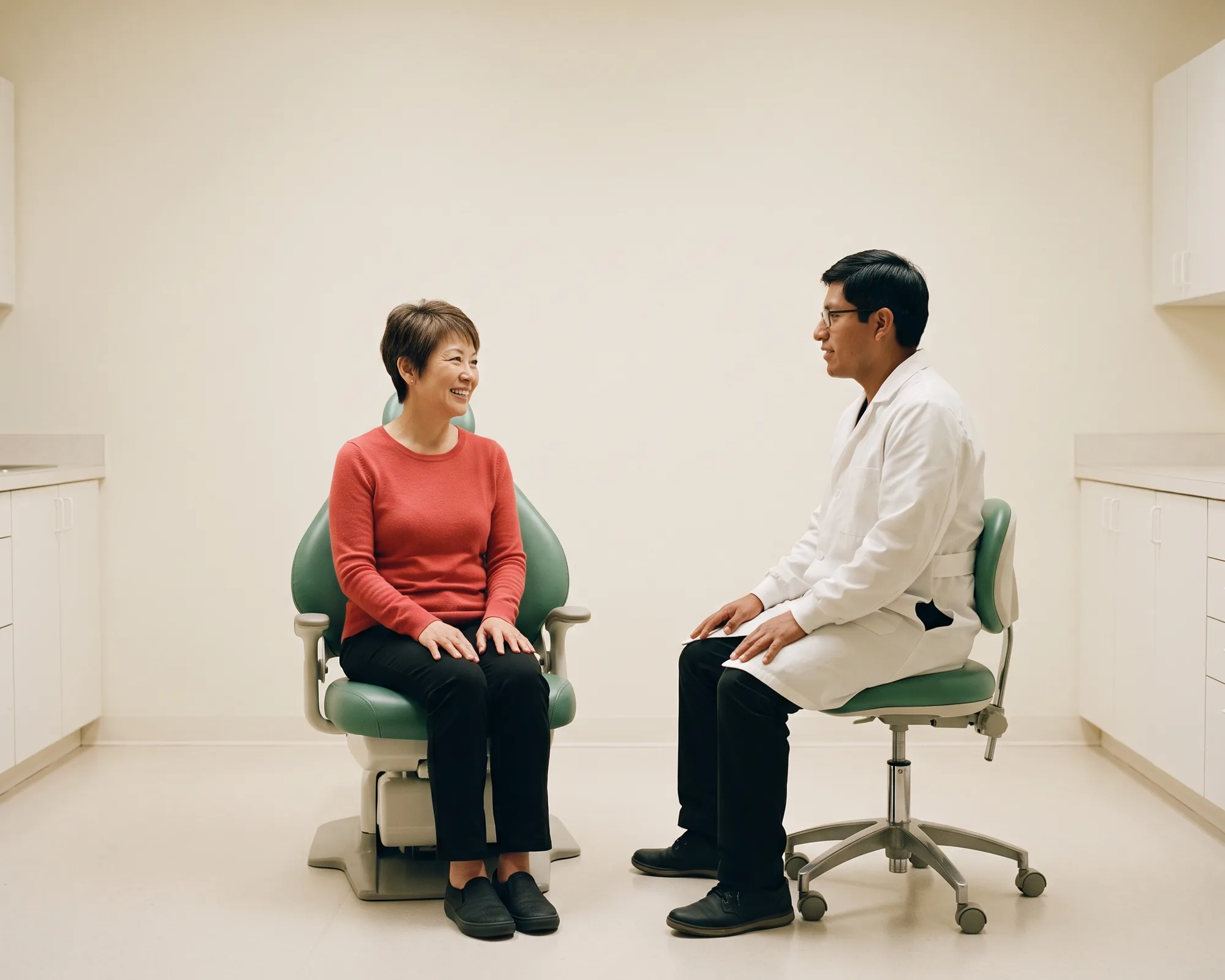 Illustrative dental conversation with a smiling woman with a short pixie cut in a coral red knit top and a dentist in a white coat.