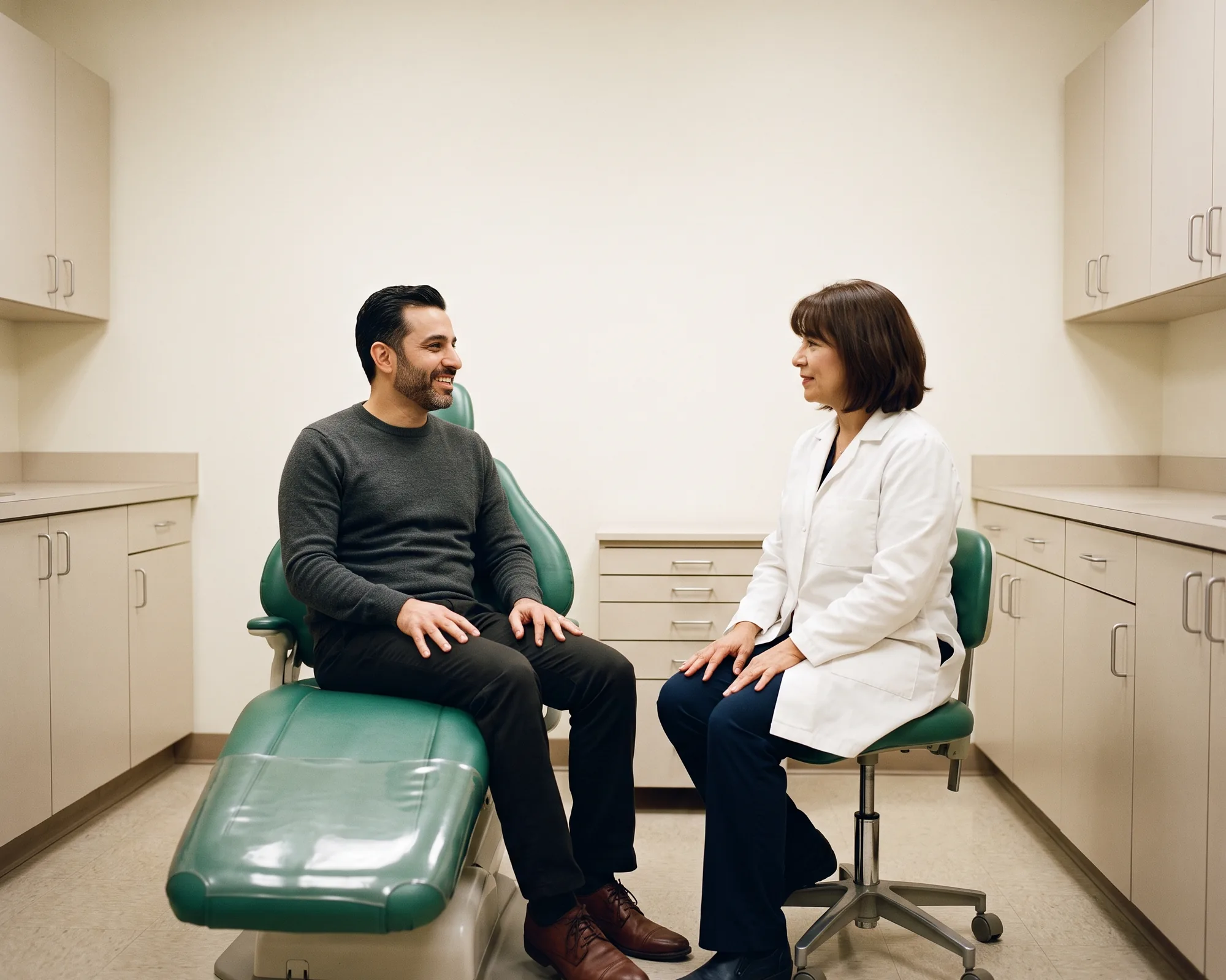 Illustrative dental conversation with a smiling bearded man in a charcoal sweater and a dentist in a white coat.