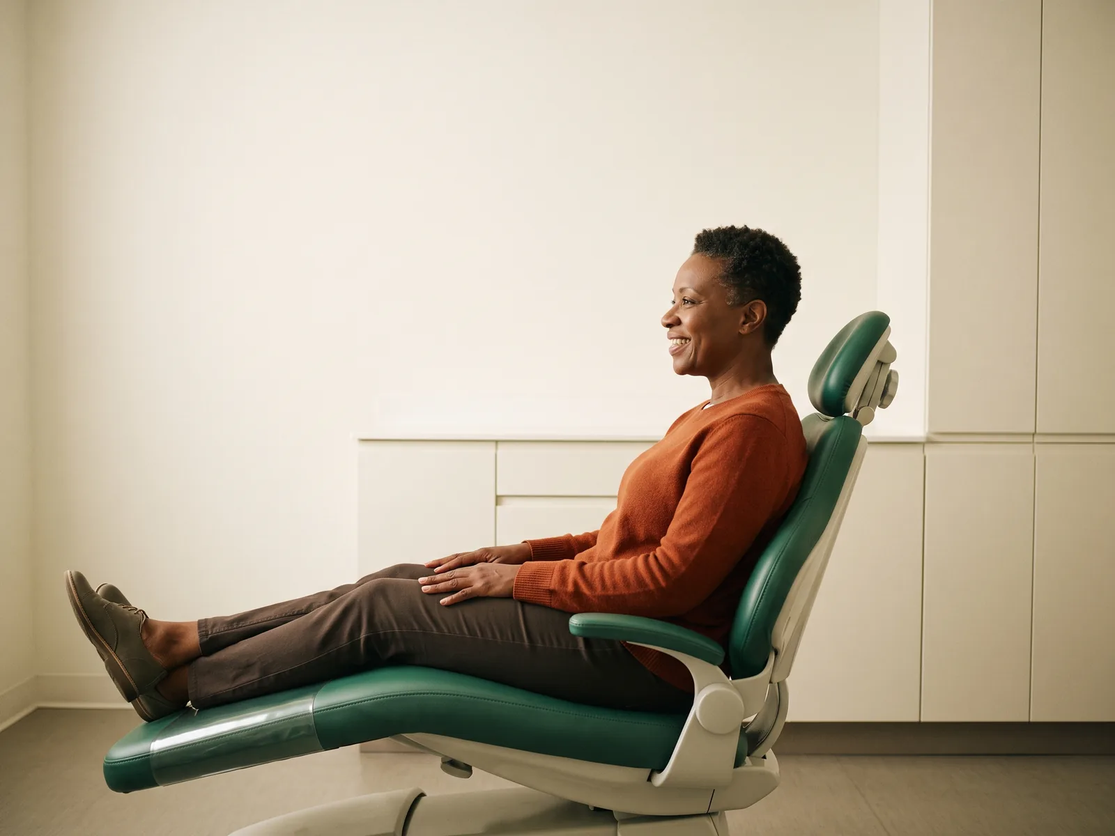 Illustrative image of a smiling woman in a rust-orange sweater reclining in a dental chair.