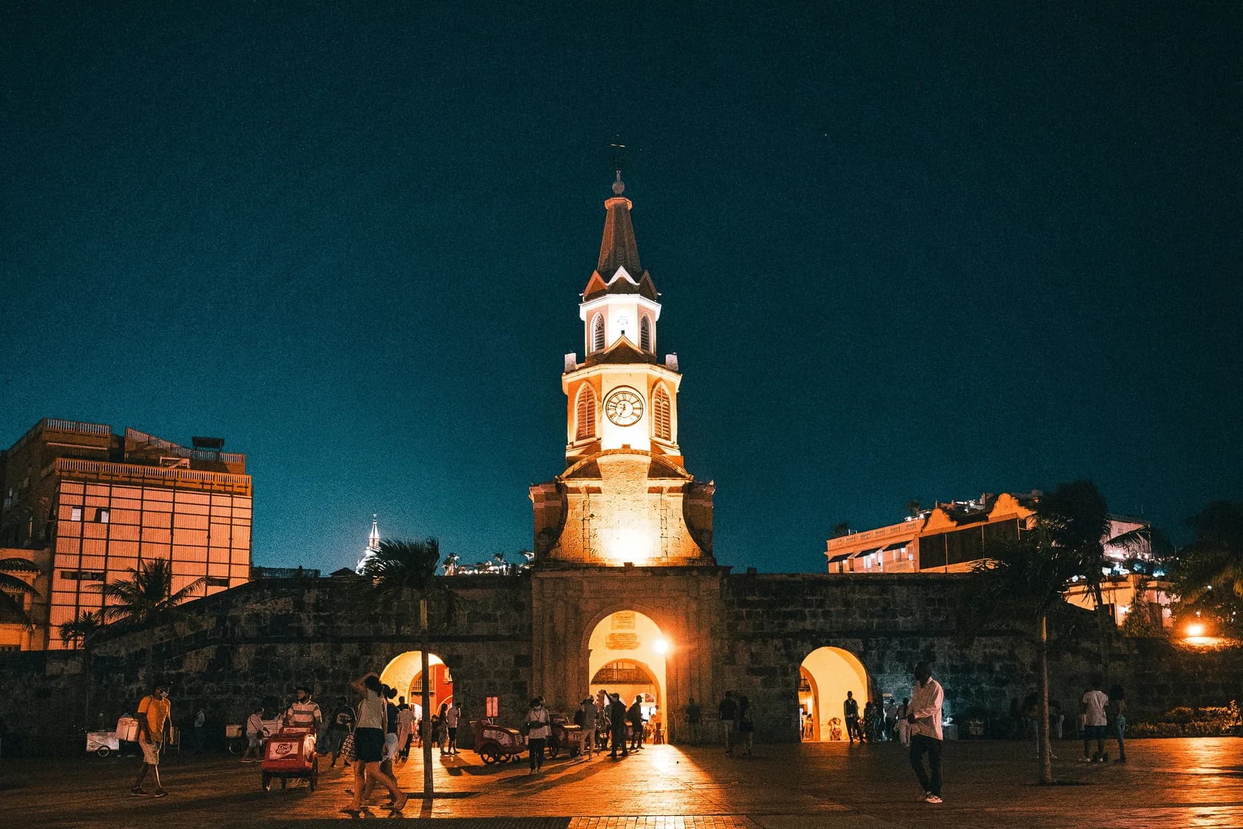 The illuminated Torre del Reloj rises above the stone entrance to Cartagena’s walled city at night.
