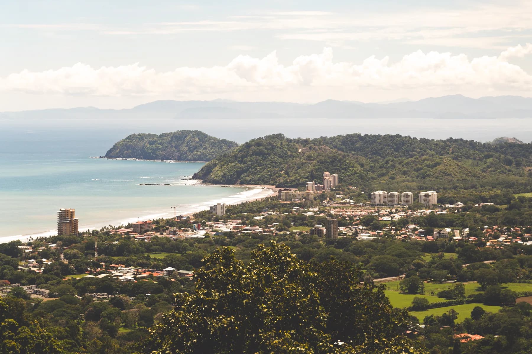 Jacó Beach and its curved Pacific shoreline bordered by green hills in Jacó, Costa Rica.