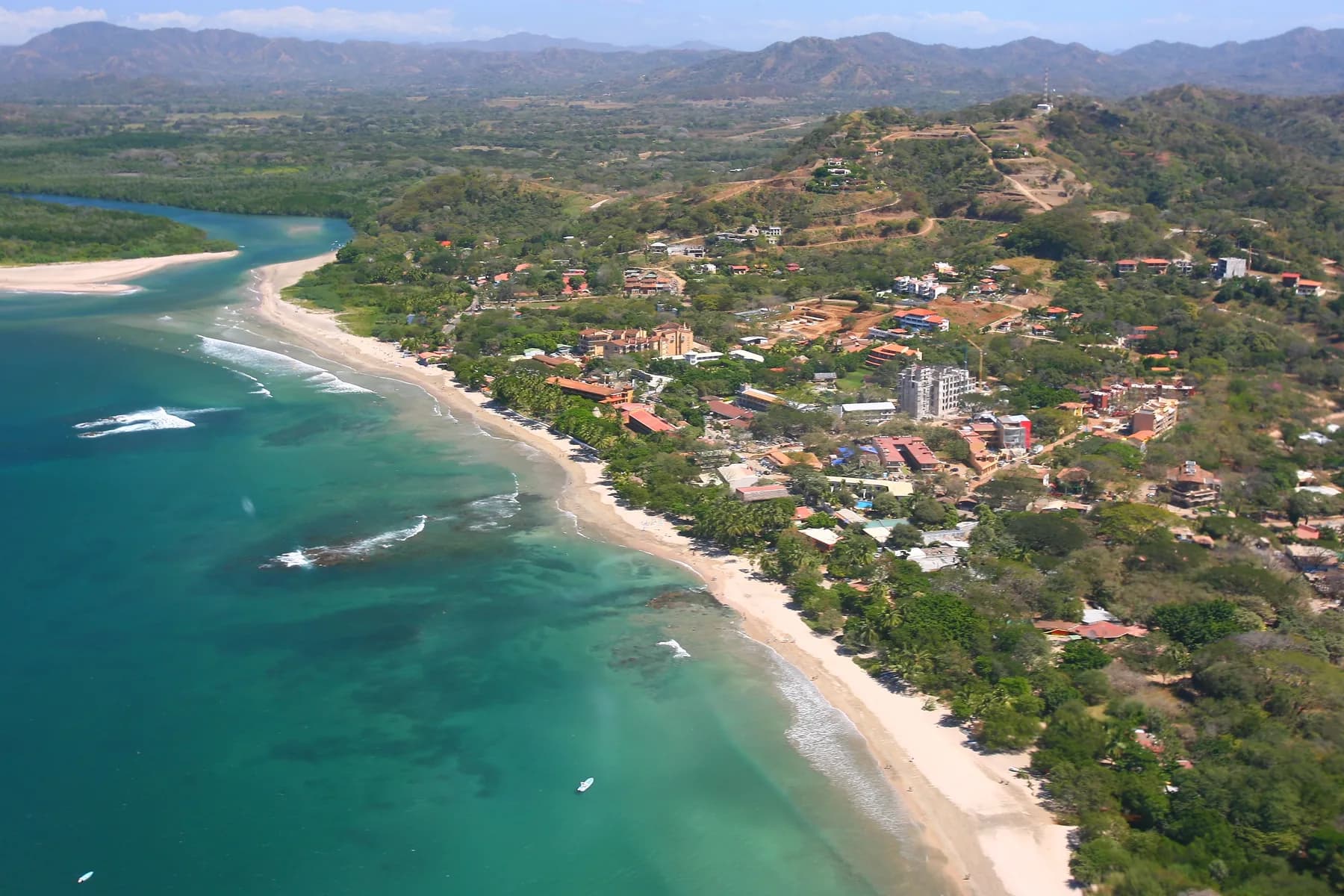 Tamarindo Beach and the Tamarindo River mouth curve beside the town and green hills in Tamarindo, Costa Rica.
