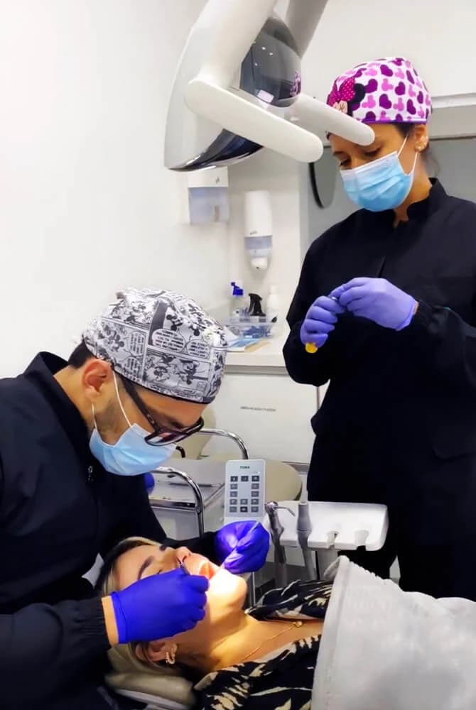 Two masked clinical workers beside a reclining patient in a dental operatory